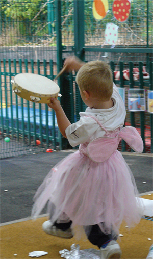 Boy plays a tambourine as he runs around in a fairy costume