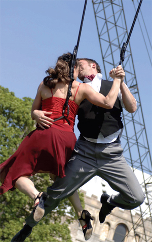 A couple in harnesses in the air, embrace, as part of a performance piece