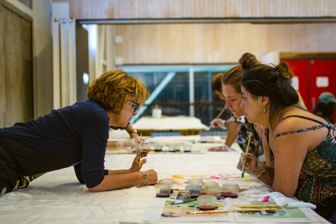 Photo of three artists leaning over a desk with artwork