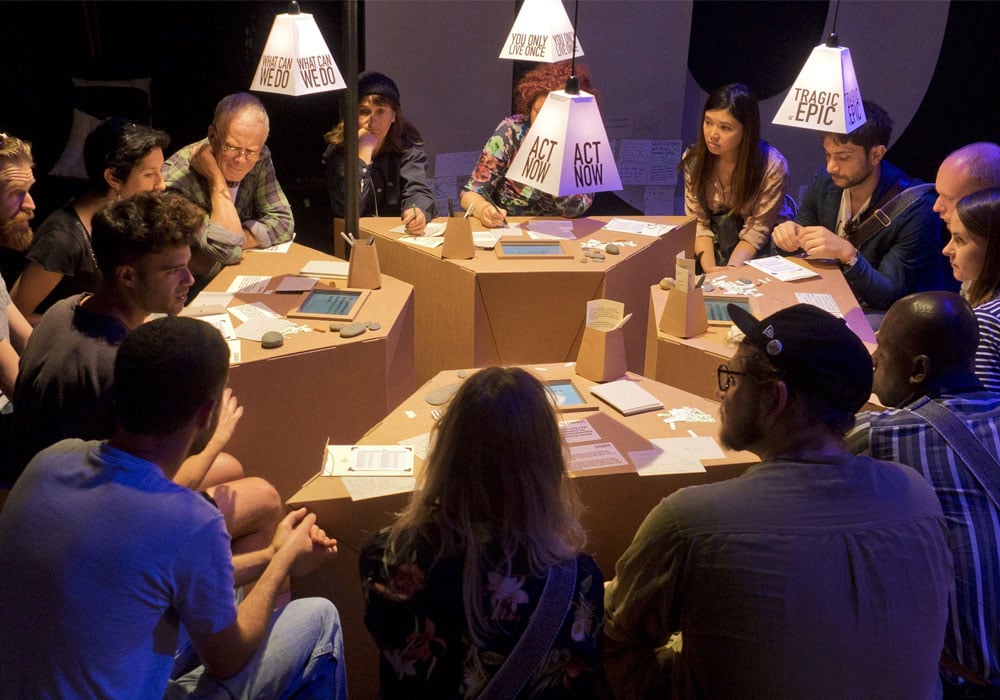 Photo of an interactive installation, a group of people meet around cardboard tables