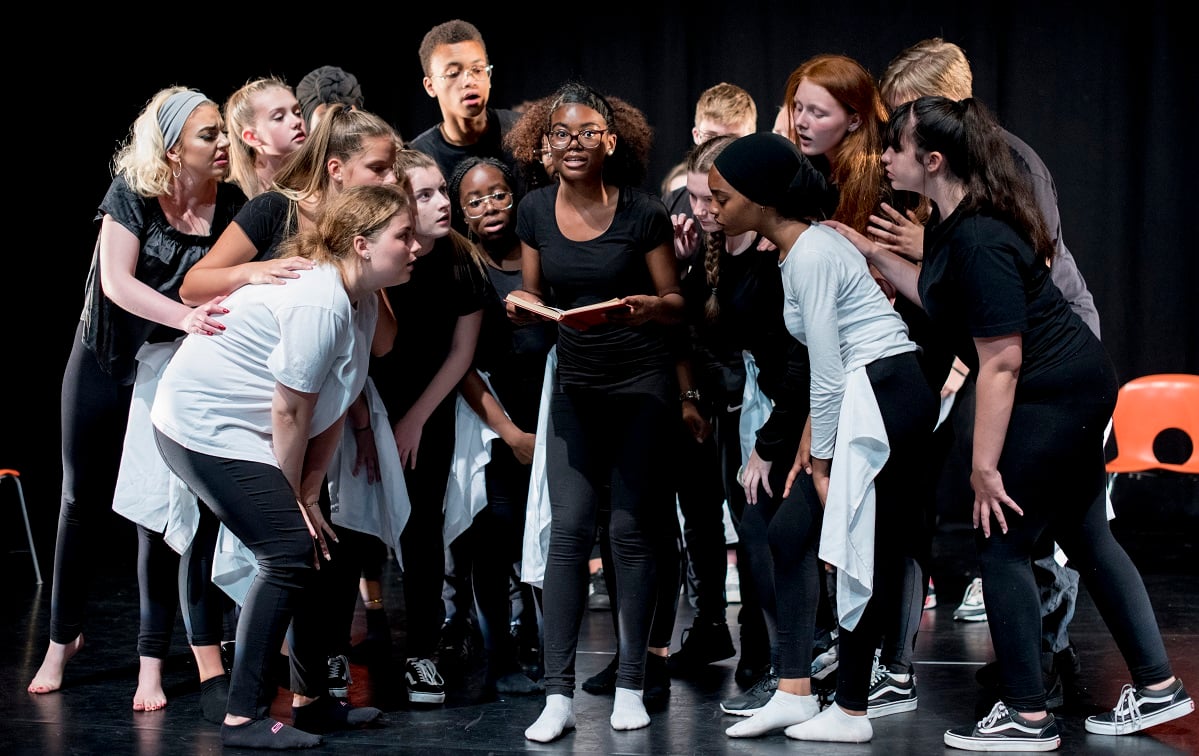 A photo of young people gathered around a young woman holding a book