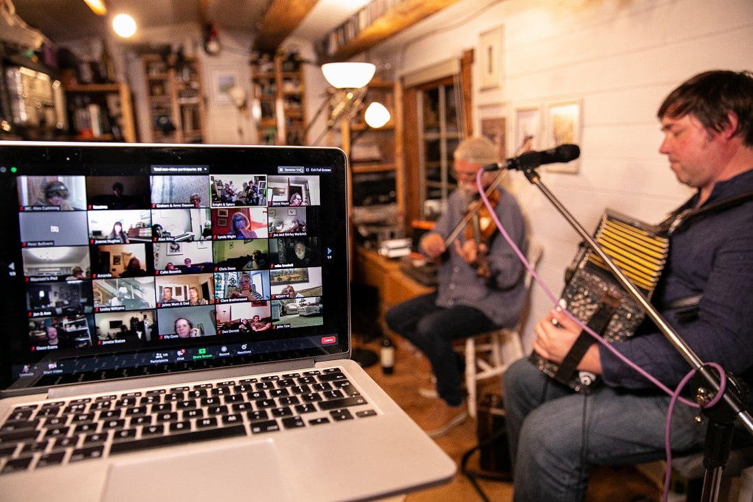 Laptop confrence call screen in the foregrounf and two musicians in the background