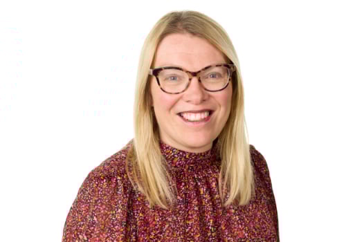 Beckie Hart, Chair of the Board 2023. She is a white woman wearing a flower-patterned pink, turtleneck shirt. She wears round, tortoise shell glasses and pink lipstick. She has mid-length, blonde hair and green eyes. The background is white.