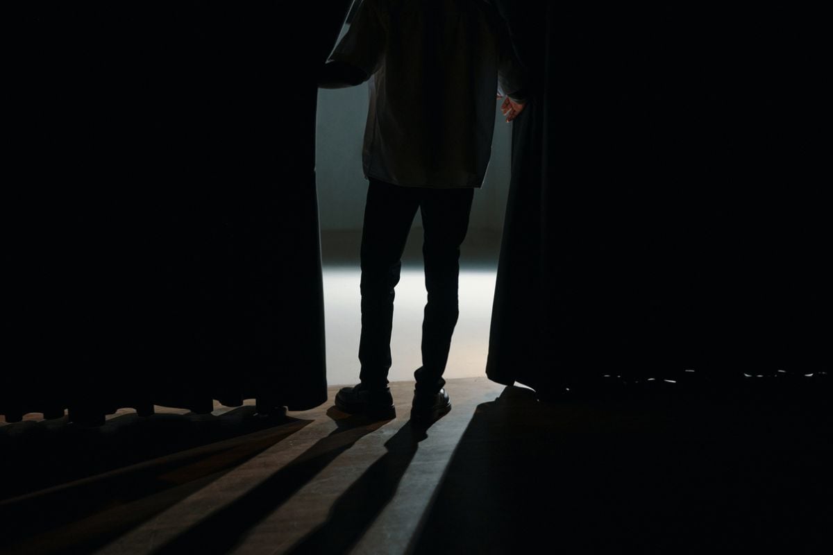 Showcasing silhouette of person entering stage through dark curtains with bright spotlight ahead casting long shadows on floor

iStock