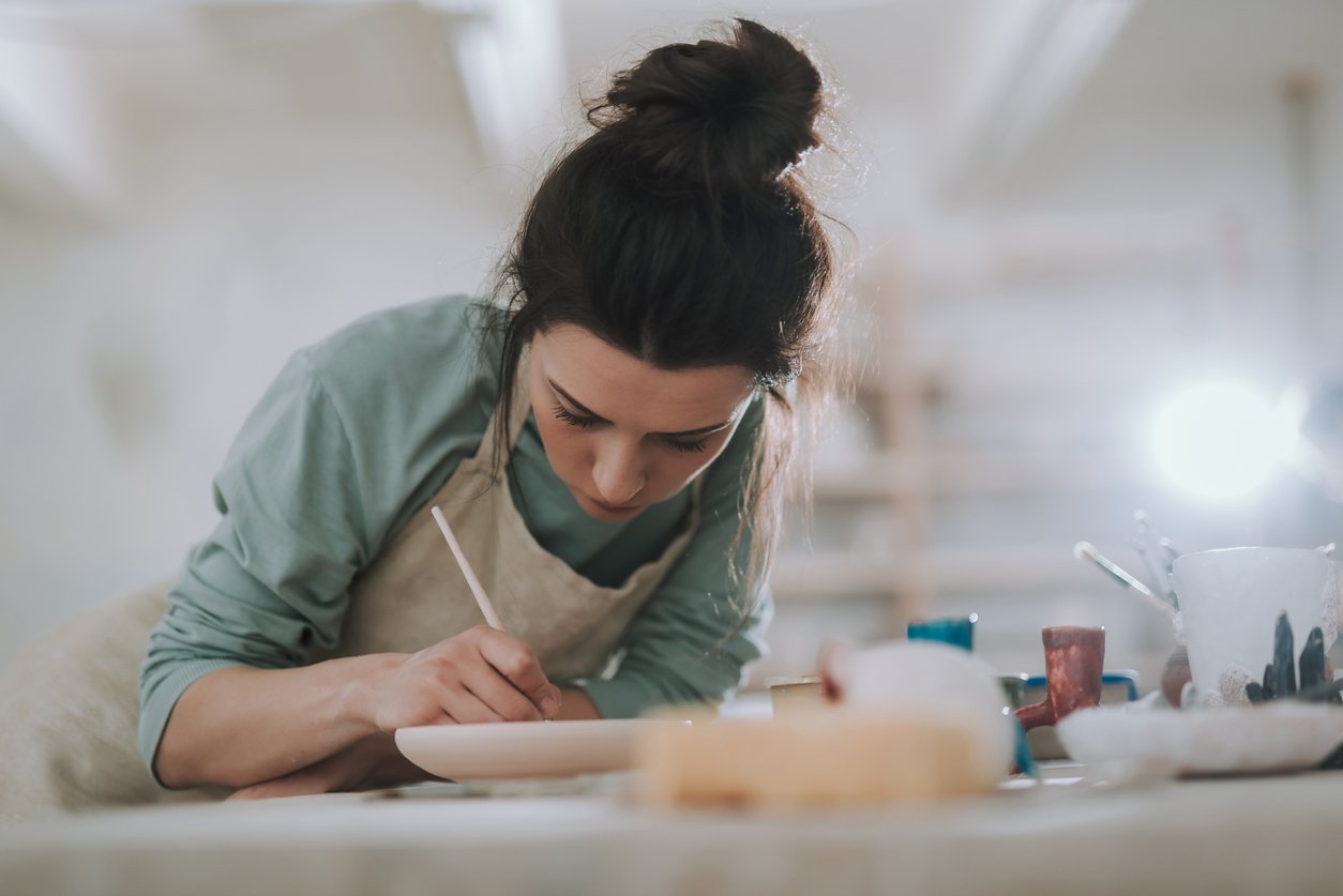 Close up portrait of beautiful female artist drawing on clay plate with serious expression