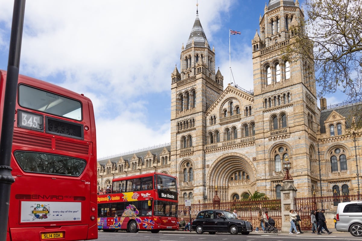A busy street scene in London featuring the historic Natural History Museum architecture and iconic red transport moving through traffic. London, UK, 7 April 2024