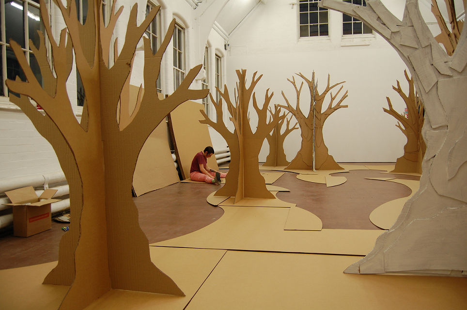 Once the trees had all been drawn, my next task was to embed them within a landscape. This was to be made from sheets of cardboard, angled at various heights to give the illusion of a fractured terrain. I decided upon three islands with sinuous paths to give a sense of discovery. Amongst the trees and busily at work is my trusted assistant Effy Harle.