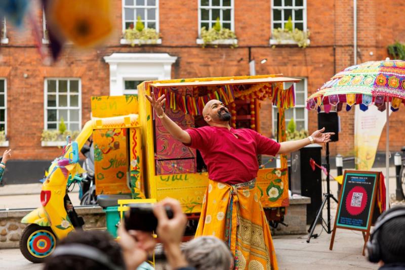 Image from Trigger's latest production, Teabreak, showcasing a person depicted dancing in front of a vibrant yellow truck while dressed in traditional attire including a flowing yellow skirt.