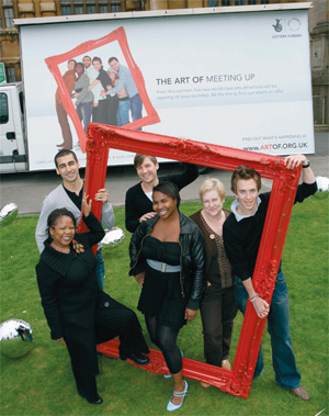People pose in front of a 'The Art of Meeting up' poster, the people are holding a big red picture frame, as if they are the picture's subject