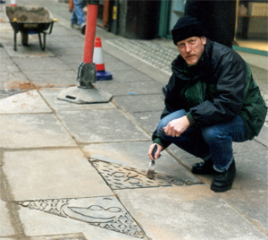 A man engraves patterns into paving slabs in the street