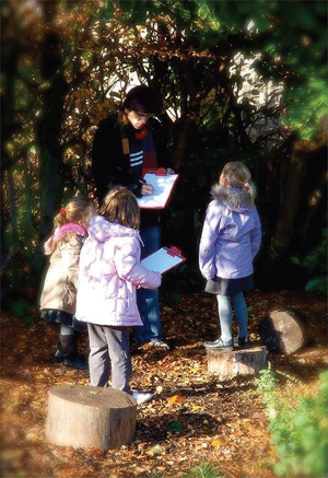 Three girls stand with clipboards, with a man, in a wood