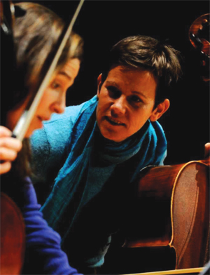 A lady cellist looks over the shoulder of another, younger, cellist