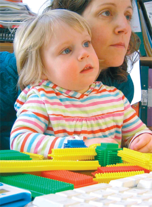 A lady sits at her desk with a child on her lap