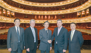 Five men (two british and three chinese) stand on stage at the Royal Opera house,  two of the men shake hands
