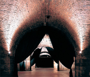 We look through three brick, indoor arches,  towards what looks to be a screen  or stage back drop.