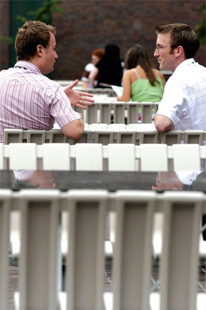 Two men sit on a bench together, one of the men appears to be explaining something to the other.