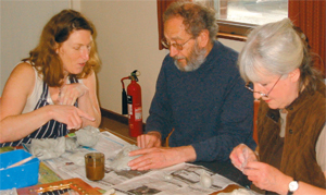 Three people sit at a table making paper mache objects