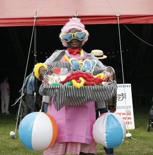 A woman dress in crazy fancy dress (includeing massive blue  haeart shaped sunglasses) stand in front of a marquis.