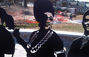 African art piece, showing a silhouetted woman in traditional dress cut out of (what looks to be) black metal.