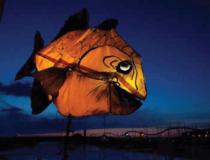 A massive illuminated and air filled yellow fish in the night sky
