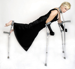 A white woman in a long black dress balanced horizontally on four crutches