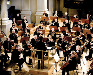 A group of orchestral musicians in a semi-circle, watching the conductor