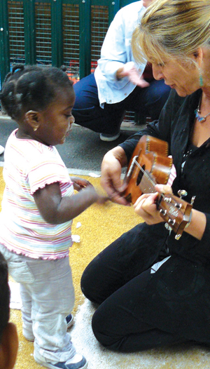 A little black girl looking at a kneeling woman playing guitar