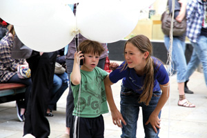 Small boy holding balloons with a taller girl crouching beside him