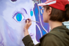 Female painter draws picture with paintbrush on canvas for outdoor street exhibition