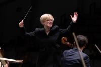 Catherine Larsen-Maguire, incoming Music Director, NYOS. She is captured conducting with her arms in the air holding a baton.