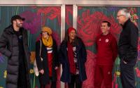 group of people stand in front of a murial