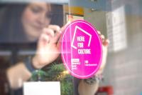 A woman places a pink Culture Recovery Fund sticker on the window of a venue