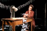 Theatre maker Viv Gordon performs Cutting Out. Viv is sat at a table cutting out images with a pair of scissors. She is wearing a brown jump suit