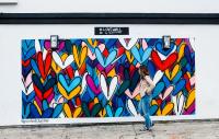 Woman walking past graffiti of multicoloured hearts