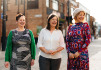 (L to R) Janine Crombie (Development and Communications Director), Joanne Norman (Finance and Operations Director), Marianne Lewsley-Stier (Creative Director). They stand outside, all laughing. They are in focus and the background is blurred.