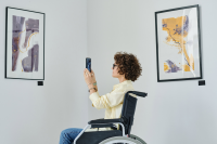 women in a wheelchair takes a photo of artwork in a museum