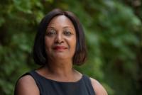 Jennifer Francis, incoming Director of External Affairs at the Museum of London, is a Black woman with short, dark hair, standing outside in front of trees. The background is blurred. She wears black attire and red lipstick.