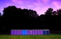 a row of portable toilets in a field, photo taken at twilight