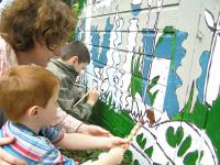 Photo of a woman and children painting a mural