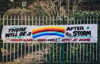 banner on railings with the words "there will be a rainbow after the storm" (the word 'rainbow' is replaced with a painting of a rainbow)