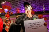 Face-painted man with sign: 'Celebrating the dead, silencing the living'