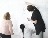 Photo of three women drawing on a white wall