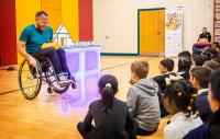 A man in a wheelchair performing for a group of young children