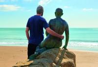 Photo of man on beach with arm round sculpture