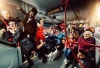 'Back to Ours' company photo. A diverse range of people photographed from the inside of a bus. There are people sat down and stood up. Some are performing, others are smiling and gasping.