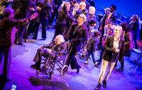 casual group of people on a stage with an elderly person in a wheelchair in the foreground