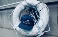 a baseball cap lodged in a life buoy on a boat. The caption on the hat is "harmonize humanity"