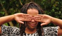 A Black person covering their each eye with their hands, palms facing towards the camera