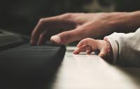 An adult's and child's hand on a piano keyboard