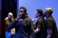 PROJEKT ENCOUNTER at The Marlowe Theatre, February 2023. Image focuses on a Black man wearing a Black zip-up hoodie performing with his hand in front of his mouth, as he looks at the camera.